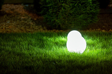 backyard garden light with lantern electric lamp with sphere diffuser in green grass with thuja...
