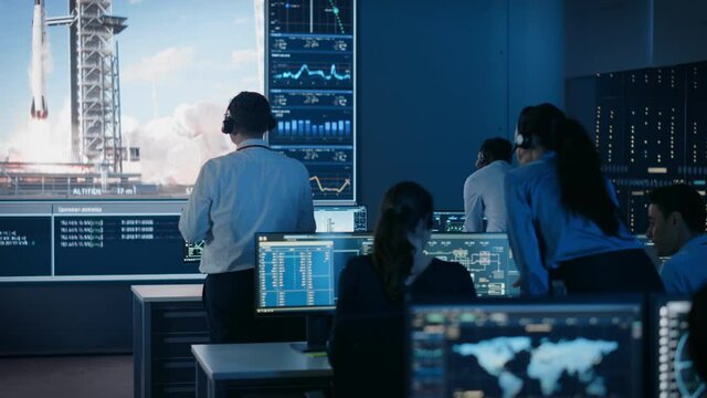 Group of People in Mission Control Center Witness Successful Space Rocket Launch. Flight Control Employees Sit in Front Computer Displays and Monitor the Crewed Mission. Team Stand Up and Clap Hands.