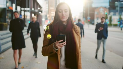 Beautiful Young Woman Uses Smartphone with Animated Social Media Icons Flying Away, Walks on Crowded City Streets. Social Network Concept, Likes, Emoticons, e-business. Front View Following Shot 
