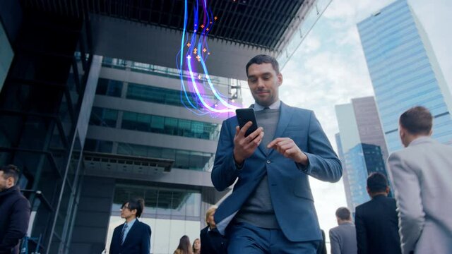 
Handsome Businessman Uses Smartphone with Animated Abstract Digital Data Lines Flying, Walks on Crowded City Streets. Big Data, Information, e-Business Concept. Low Angle Front View Following Shot