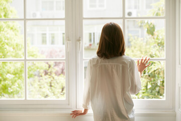 rear view of a young asian woman staying at home looking out of winow