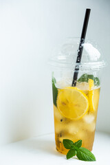 Green tea with iced lemon and lemon balm in a plastic glass on a white background