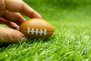 Hand is holding American Football on green grass background