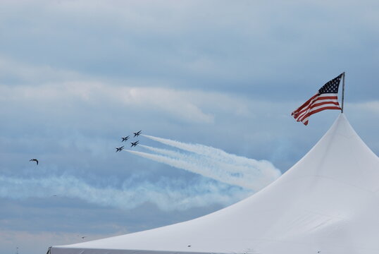 Four of the U.S. Navy Blue Angels flight demonstration squadron speed past a tent with the American flag. 