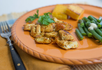 Curried cubes of chicken breast and funchi (corn meal mush or polenta) served on an orange plate with green beans. 