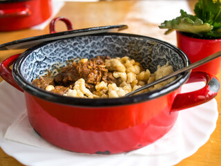 Bright red enameled pot full of goulash and späztle in Austrian restaurant. 