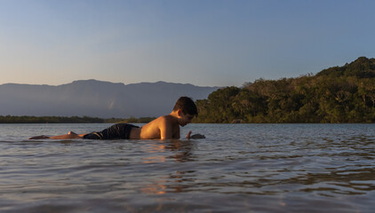 Menino brincando e se divertindo nas águas limpas do rio em linda tarde com por do sol