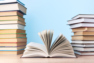 An open book and two stacks of books are on a wooden table against a light blue wall, a place for text