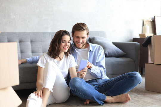 Happy couple sitting and planning new home decoration at home with a smartphone at moving day, renovation and interior design for new house