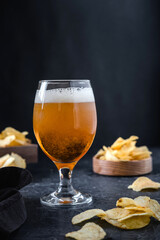 Glass of beer and chips on dark background. Cold beer in a long glass.