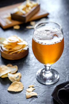 Glass of beer and chips on dark background. Cold beer in a long glass.