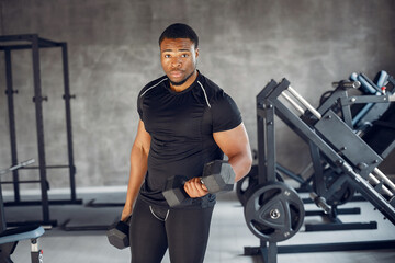 Fototapeta na wymiar Sports man in the gym. A black man performs exercises. Guy in a black t-shirt