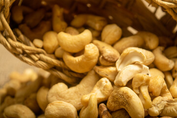 Cashew nuts in a wicker basket and cashew nuts scattered on burlap with a rough texture surface texture. Close up.