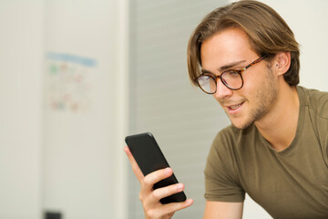 a smiling handsome young man wearing glasses checking his phone. Communication and leisure concept.