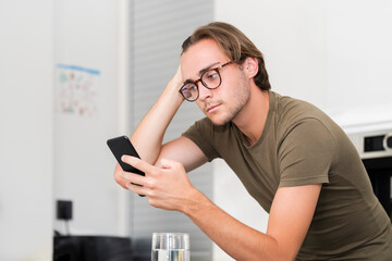 young man wearing glasses fixing his hair while using his phone. Communication and leisure concept.