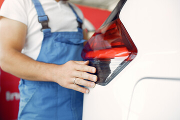 Wrker in a car salon. Expert checks the car. Man in a blue uniform.