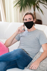 Fototapeta premium young man wearing a face mask sitting on a sofa and talking on his phone. communication concept.