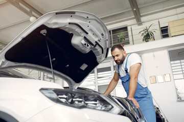 Wrker in a car salon. Expert checks the car. Man in a blue uniform.