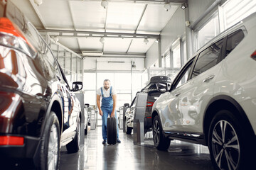 Wrker in a car salon. Expert checks the car. Man in a blue uniform.