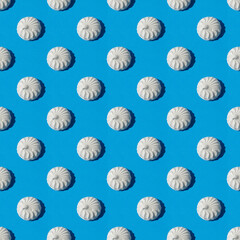 Repeating pattern of marshmallows on a light blue background. There are harsh shadows. Candy and food themes.