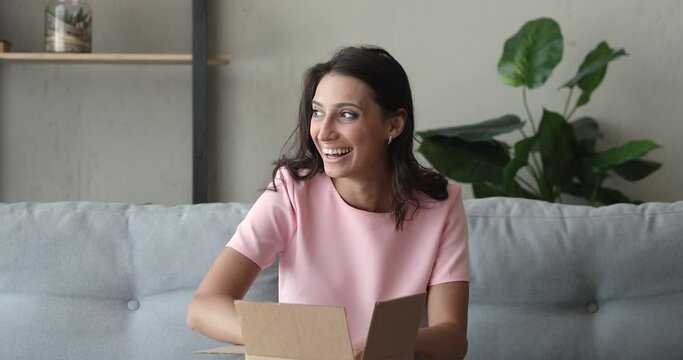 Pretty Indian woman customer sit on sofa unpack package open parcel. Girl consumer receive purchased goods in online shop feels happy, post mail shipping, prepare delivery for send to relative concept