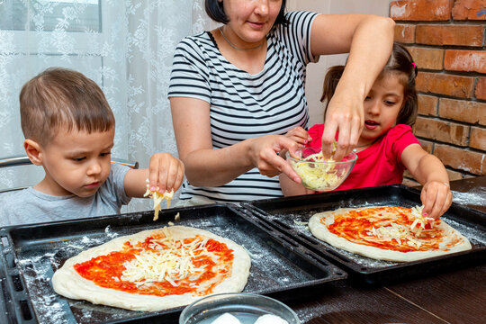 little boy and girl helping mom make pizza at home