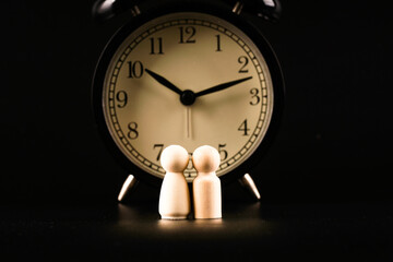 couples of wooden peg dolls over dark background with an alarm clock