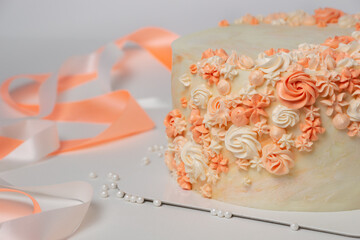 Vanila wedding cake with cream flowers decoration on light background with white, orange ribbons. Event celebration consept.