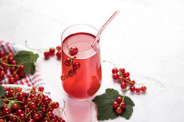Sprigs of red currant berries lie in a wicker plate on a sackcloth, a berry Morse stands in a glass glass on a light background. Summer drink that quenches your thirst