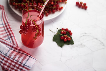 Sprigs of red currant berries are lying on a white plate, a berry Morse stands in a glass glass on a light background, next to a napkin in a red and white check. Summer drink that quenches your thirst