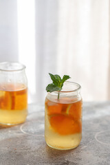 Homemade natural orange lemonade with ice and mint in little jar on concrete background. Refreshment drink for summer hot day. Copy space
