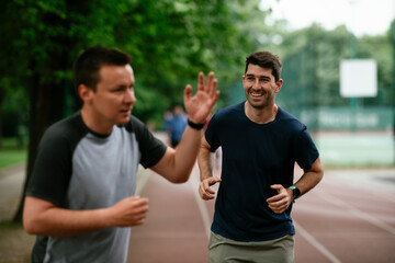 Young men training on a race track. Two young friends running on the athletics track	
