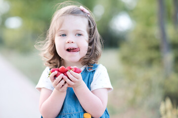 Funny baby girl 2-3 year old eating tasty strawberry outdoors closeup. Summer season. Childhood.