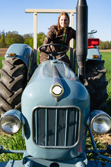 Junge Frau mit Spass an der Landwirtschaft sitzt auf einem Oldtimer - Traktor.