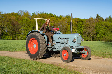 Junge Frau mit Spass an der Landwirtschaft sitzt auf einem Oldtimer - Traktor. © Countrypixel