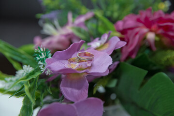 A pair of gold wedding rings . Rings on the petals of artificial pink flowers .