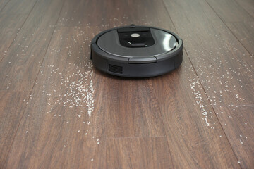 Modern robotic vacuum cleaner removing scattered rice from wooden floor
