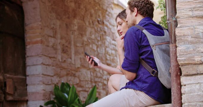 Two tourists using smartphone to search amenities or landmarks in rural town.Medium shot side view.Two people looking for hotel or restaurants on smartphone..Friends trip in Italy.4k slow motion
