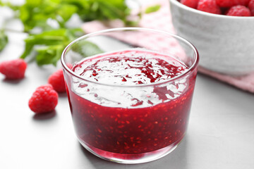 Delicious jam and fresh raspberries on grey table, closeup
