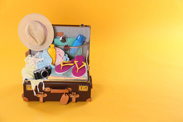 Packed vintage suitcase with different beach objects on orange background, space for text. Summer...