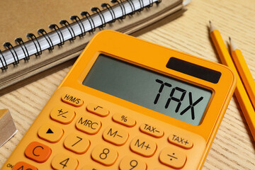 Calculator with word Tax, notebook and pencils on wooden table, closeup