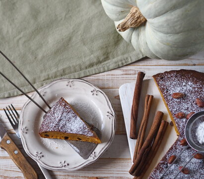 Autumn food background with healthy home cooking. Pumpkin muffin on a white wooden background with kitchen napkin, cinnamon, powdered sugar and a large pumpkin.