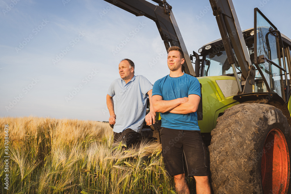 Poster ackerbau - landwirt und sohn im getreidefeld vor einem traktor blicken sorgenvoll