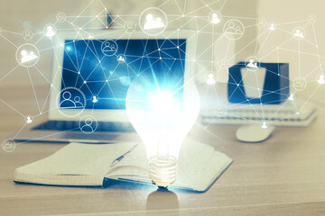 Computer on desktop in office with bulb icon hologram. Multi exposure. Concept of idea.