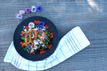 Kale salad with cherry tomatoes, carrots, pomegranate and cornflowers.