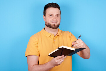 Brunette man use pen and notebook, idea concept. Isolated on blue background.