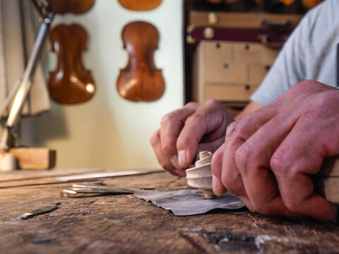 Hands of luthier violin maker carving and working on a instrument scroll in his workshop in Cremona, Italy