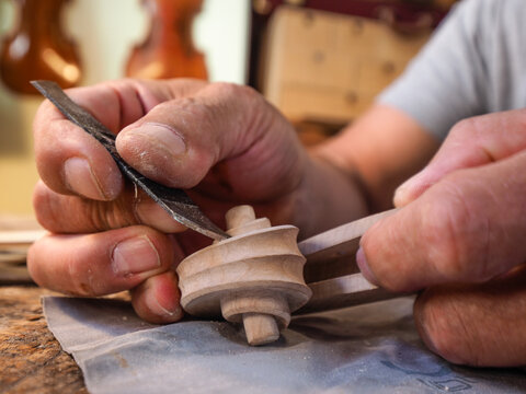 Hands of luthier violin maker carving and working on a instrument scroll in his workshop in Cremona, Italy