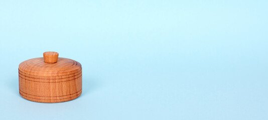 Wooden jar with cap, handmade kitchen utensil. Isolated on blue background. Copy space.