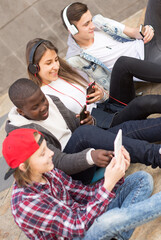 multinational teenagers play in smartphones in schoolyard